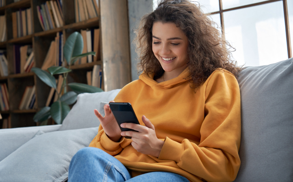 A young woman on her couch using mobile banking on her phone.