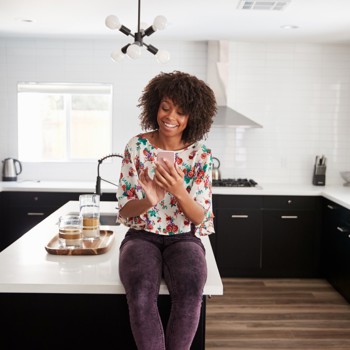 Woman banking online from her smart phone in the kitchen.