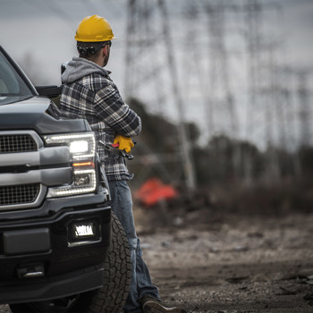 A contractor leaning on a pickup truck with high voltage electrical lines in the background.