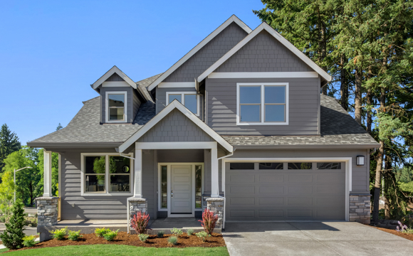 A new, modest home with mature trees and a blue sky.