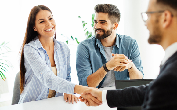 A young couple shaking hands with a mortgage loan officer. 