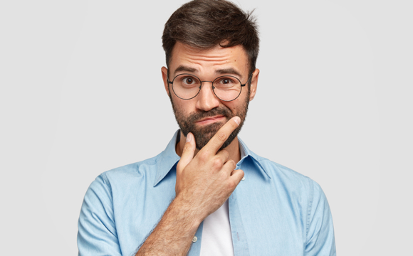 A confused looking man scratching his beard and raising an eyebrow.
