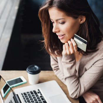 A women holding her business card near to her chin while looking at her computer.