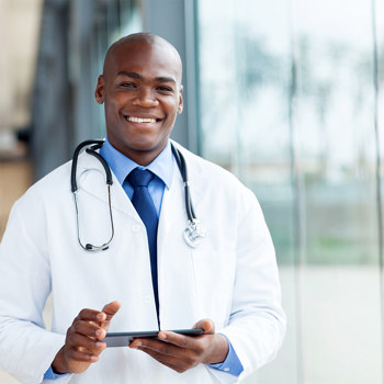 A smiling young doctor in a windowed hospital corridor