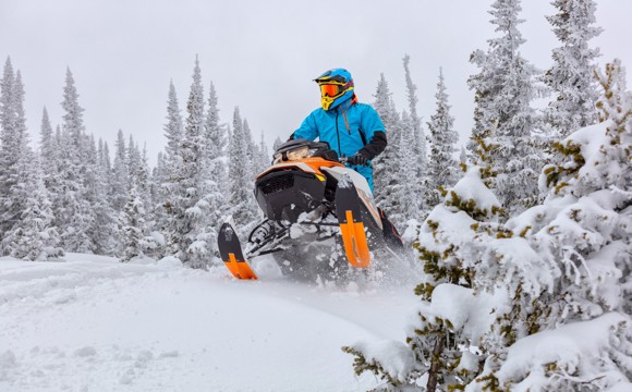 A snowmobile riding up over a snowy hill.