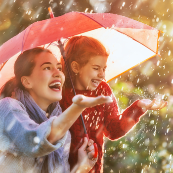 A mother and daughter standing under an umbrella in the rain