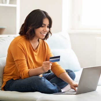 A girl sitting on her bed with her debit card and Laptop