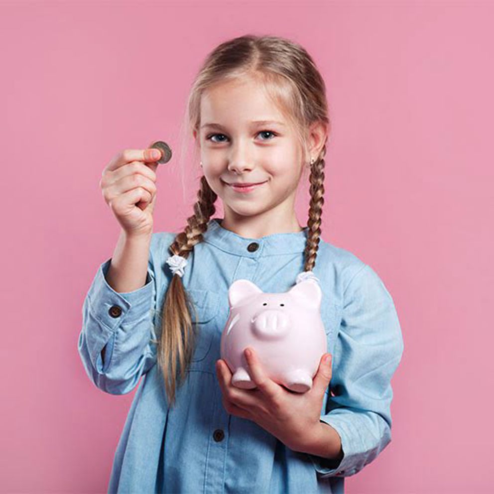 A girl holding a piggy bank and a coin in front of a pink background