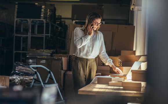 A business owner on the phone in a dimly lit shipping room.
